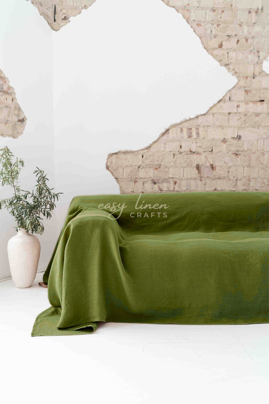 Green linen couch cover draped over a sofa with a white wall and plant in the background