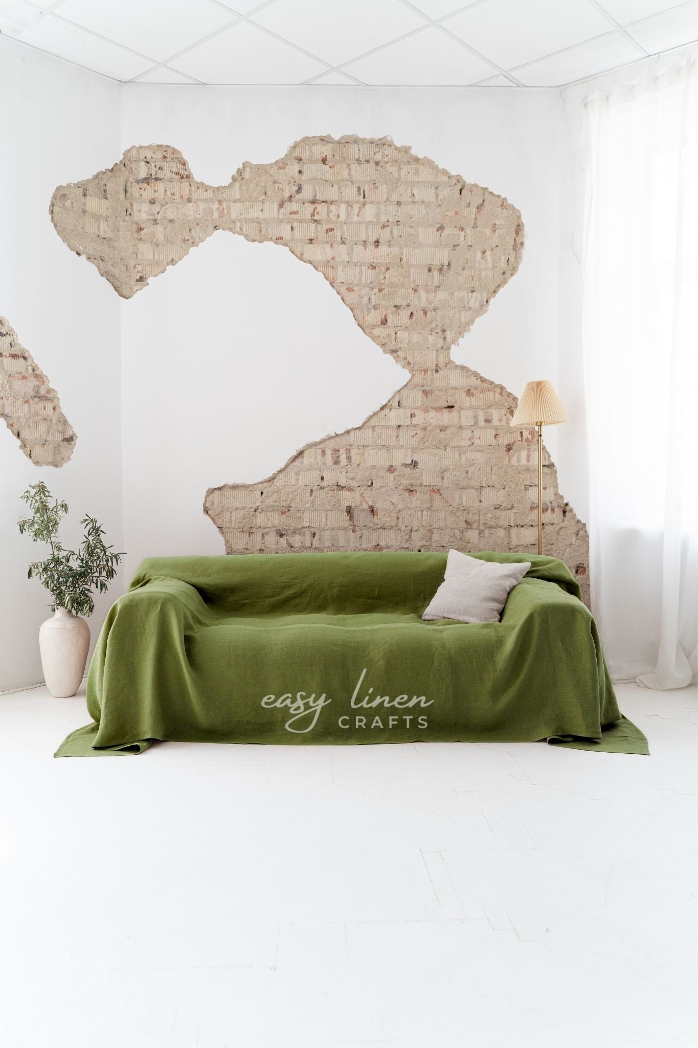 Green linen slipcover on a couch against a white wall with brick patterns.