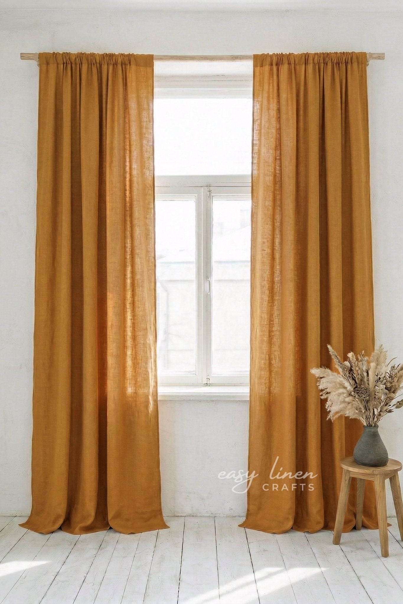 Pair of mustard yellow curtains hanging in a window with a white wall and wooden stool in the background.