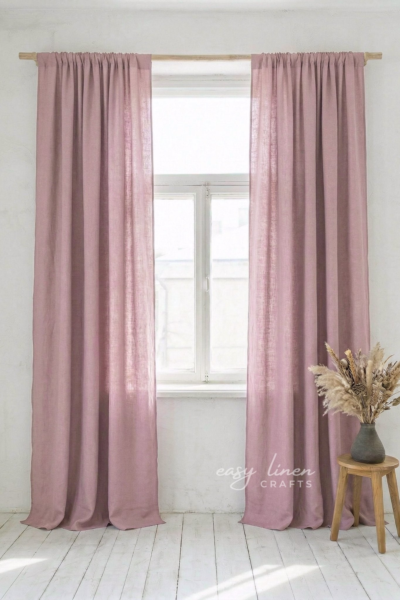 Pink curtains hanging in a window with a plant on a stool in the foreground.