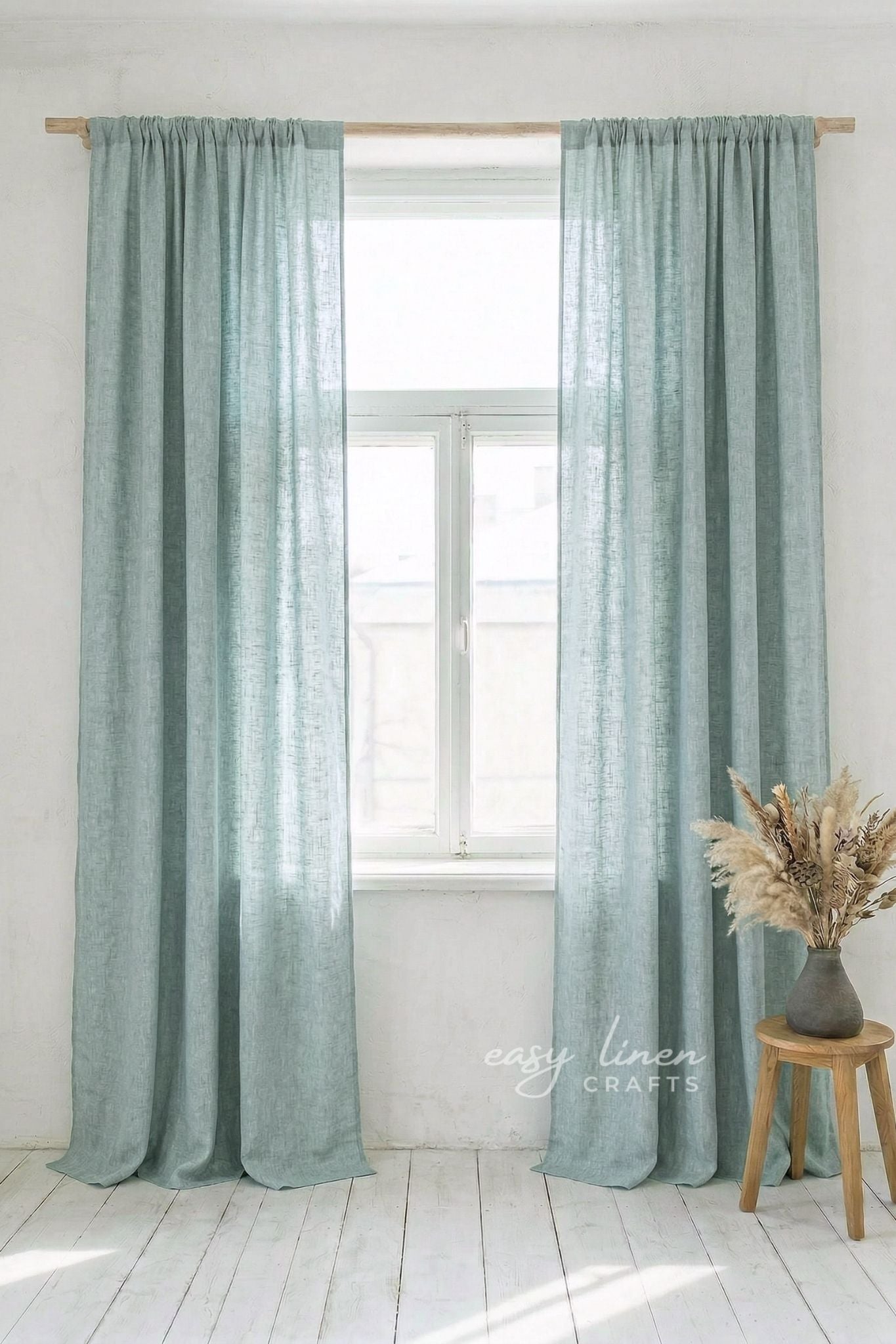 Melange Green curtains hanging in front of a window with a wooden stool and decorative vase in the foreground.