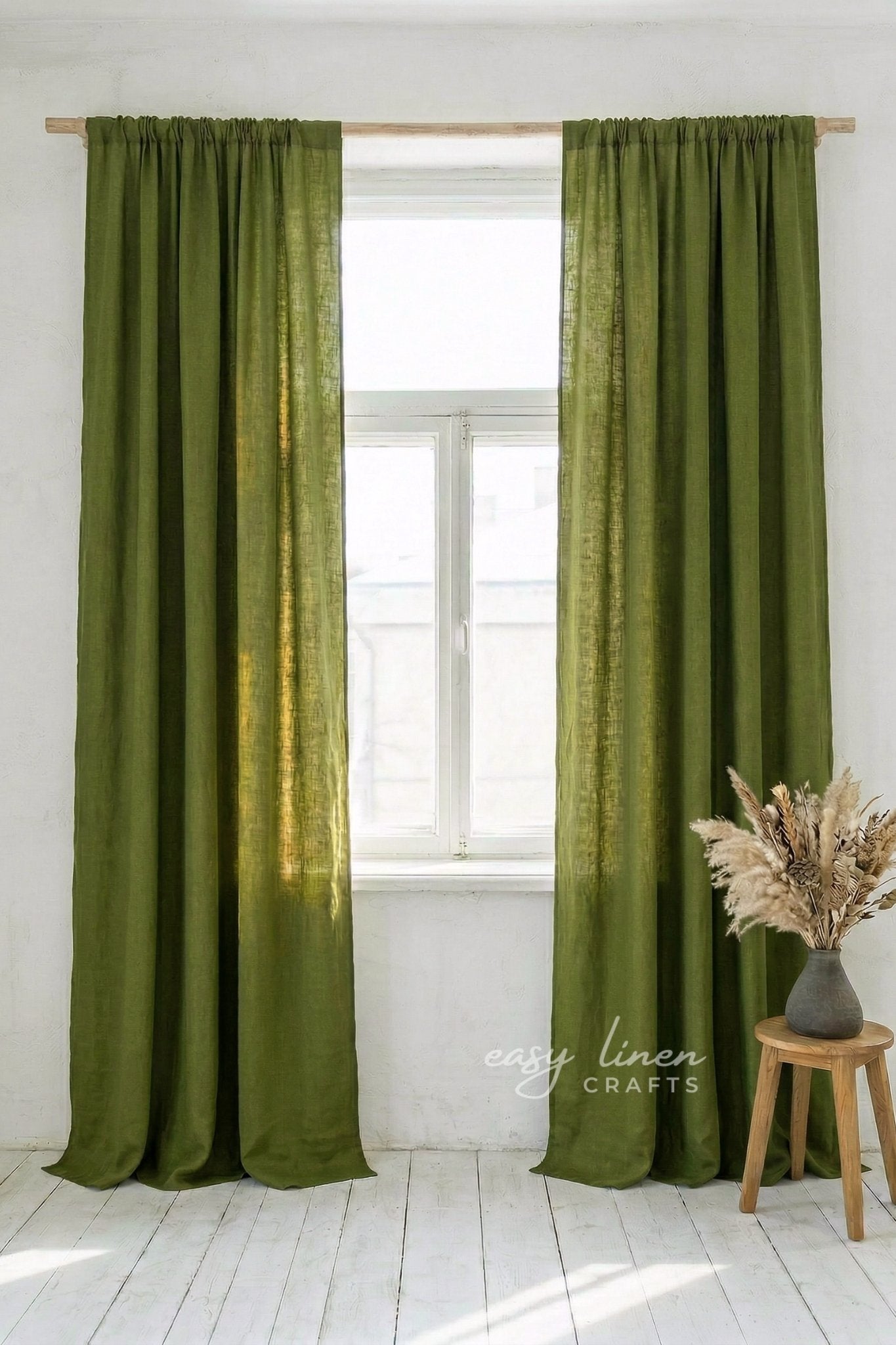 Green curtains hanging on a window with a white wall and wooden stool in the background.