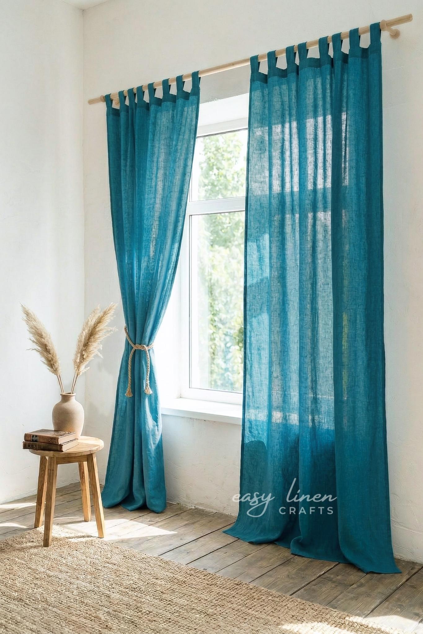Teal curtains with white tabs hanging in a room with a wooden stool and vase.