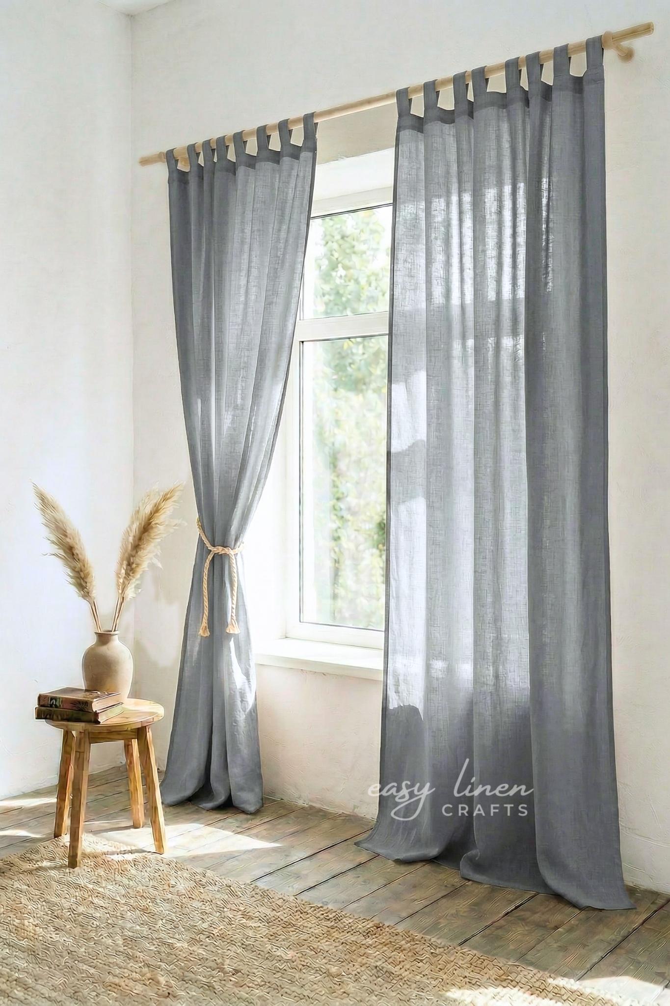 Sheer gray curtains with wooden tabs hanging in a room with a window and wooden stool.
