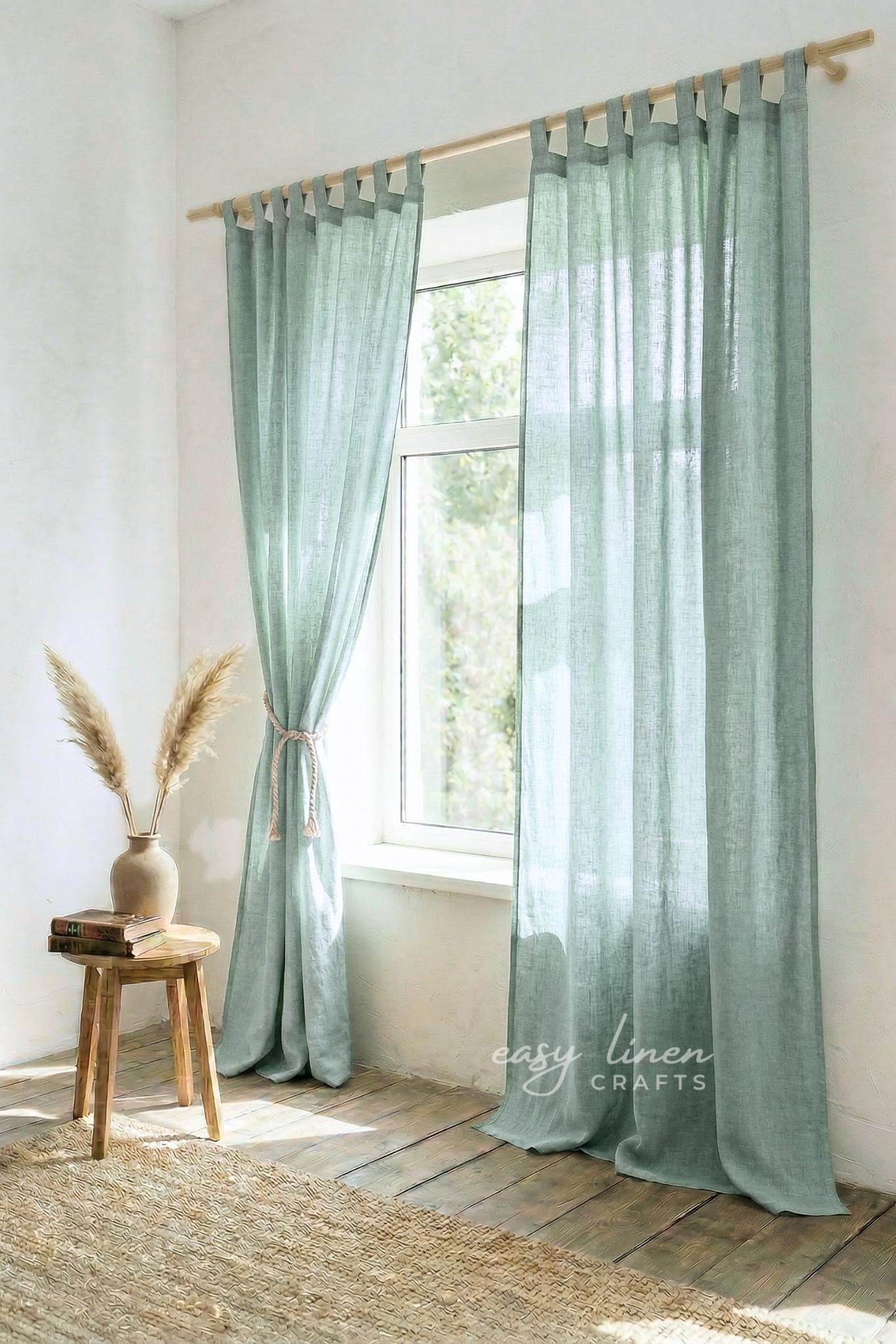 Light green curtains hanging in a room with a wooden stool and vase.