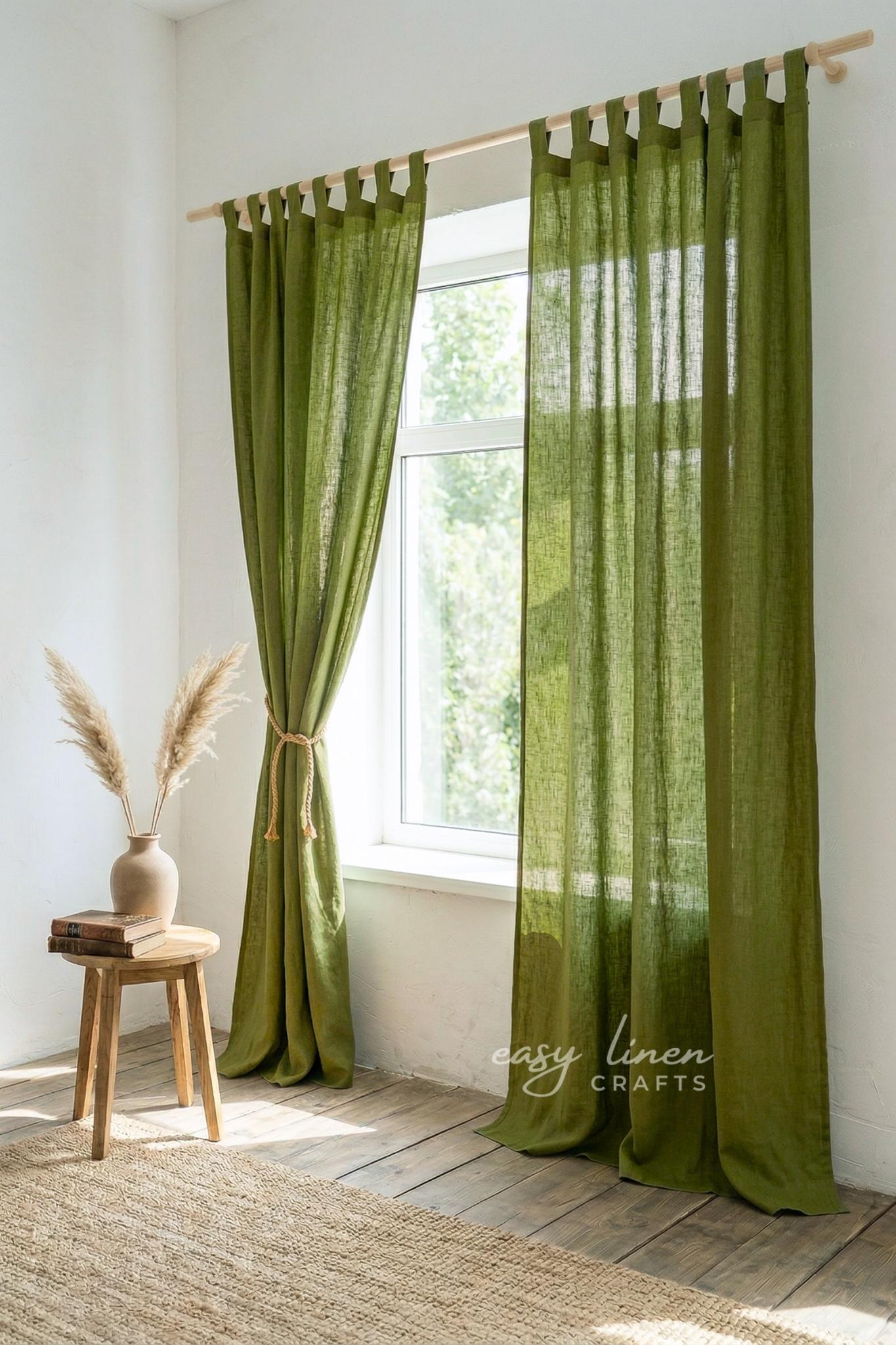 Green curtains hanging in a room with a wooden stool and vase.
