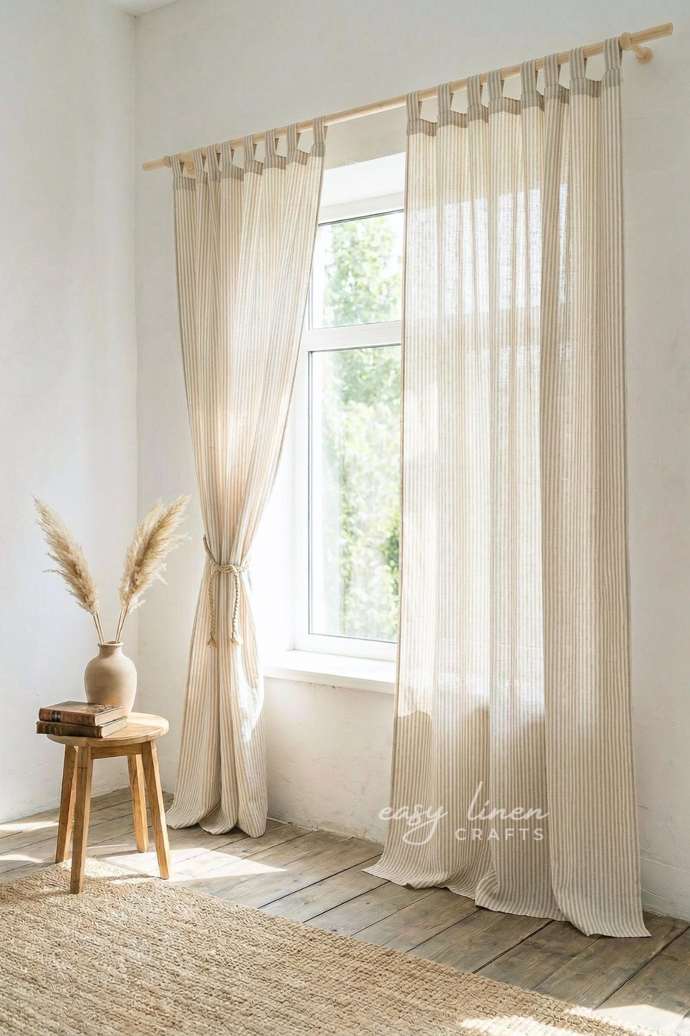 Sheer striped curtains hanging in a bright room with a wooden stool and vase.