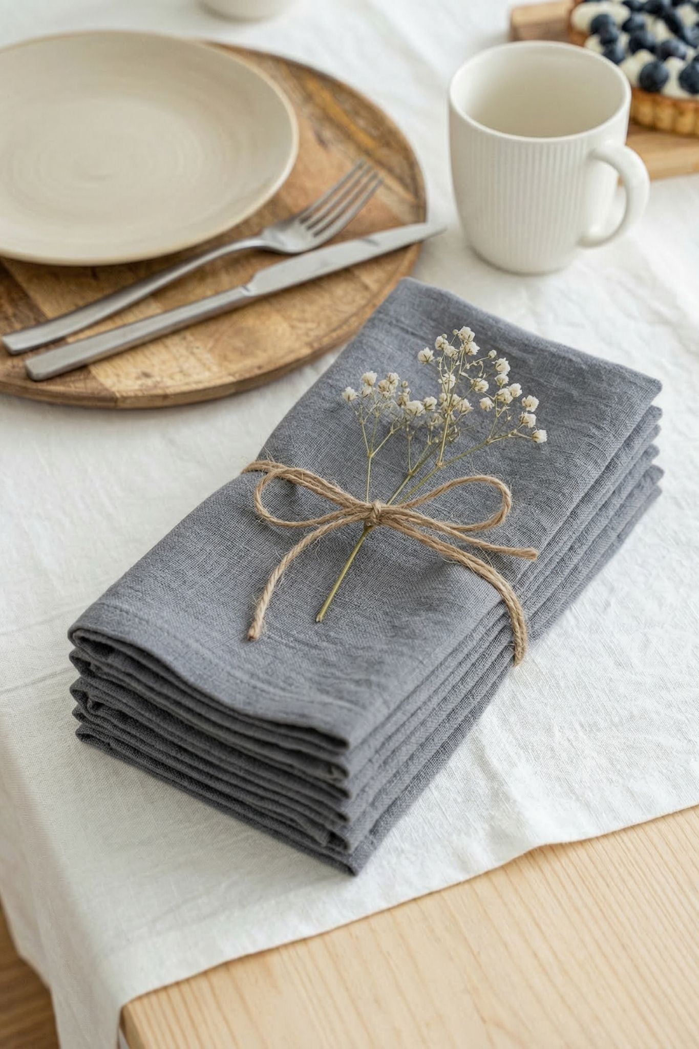 Stack of gray napkins with a small bouquet on a table setting with plates and a mug.