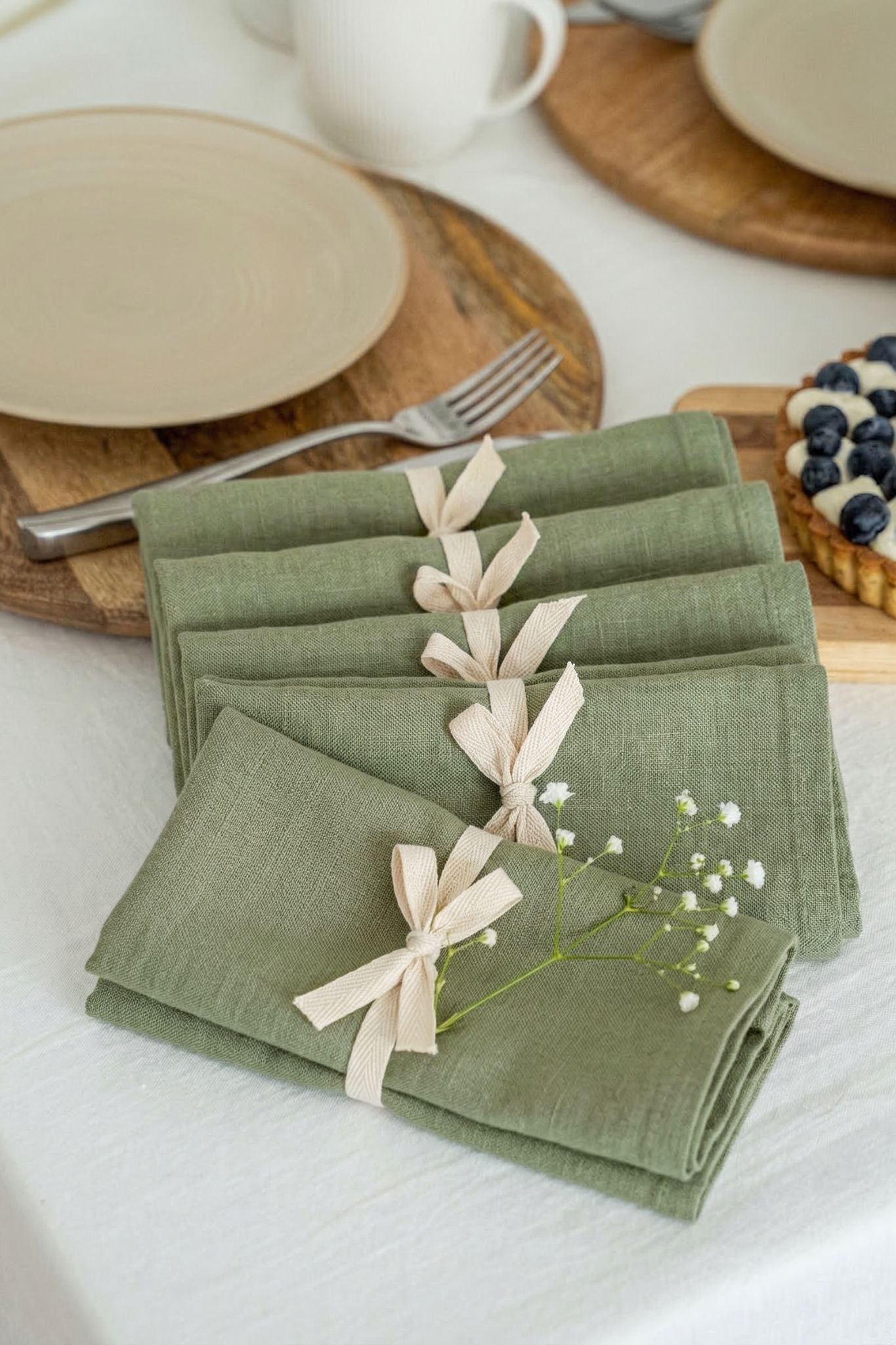 Set of green napkins with ribbons on a table setting with plates and cups.