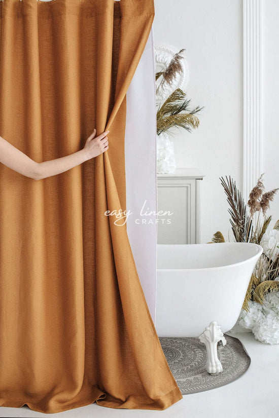 Mustard yellow shower curtain being held open in a bathroom with a freestanding bathtub and decorative plants.