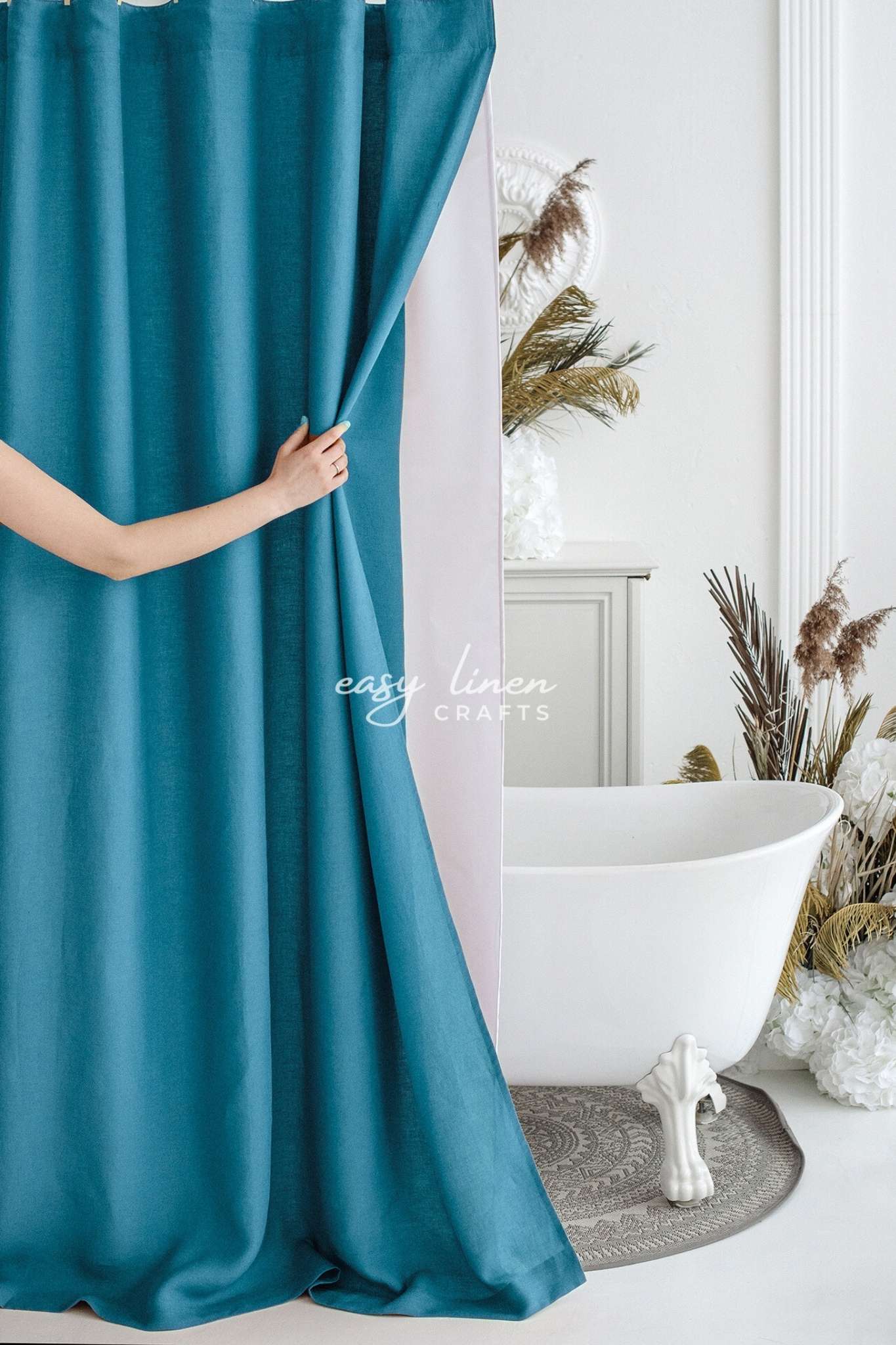 Teal blue shower curtain being held open in a bathroom with a freestanding bathtub and decorative elements.