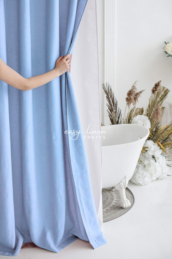 Person holding a light blue shower curtain in a bathroom with a bathtub and decorative plants.