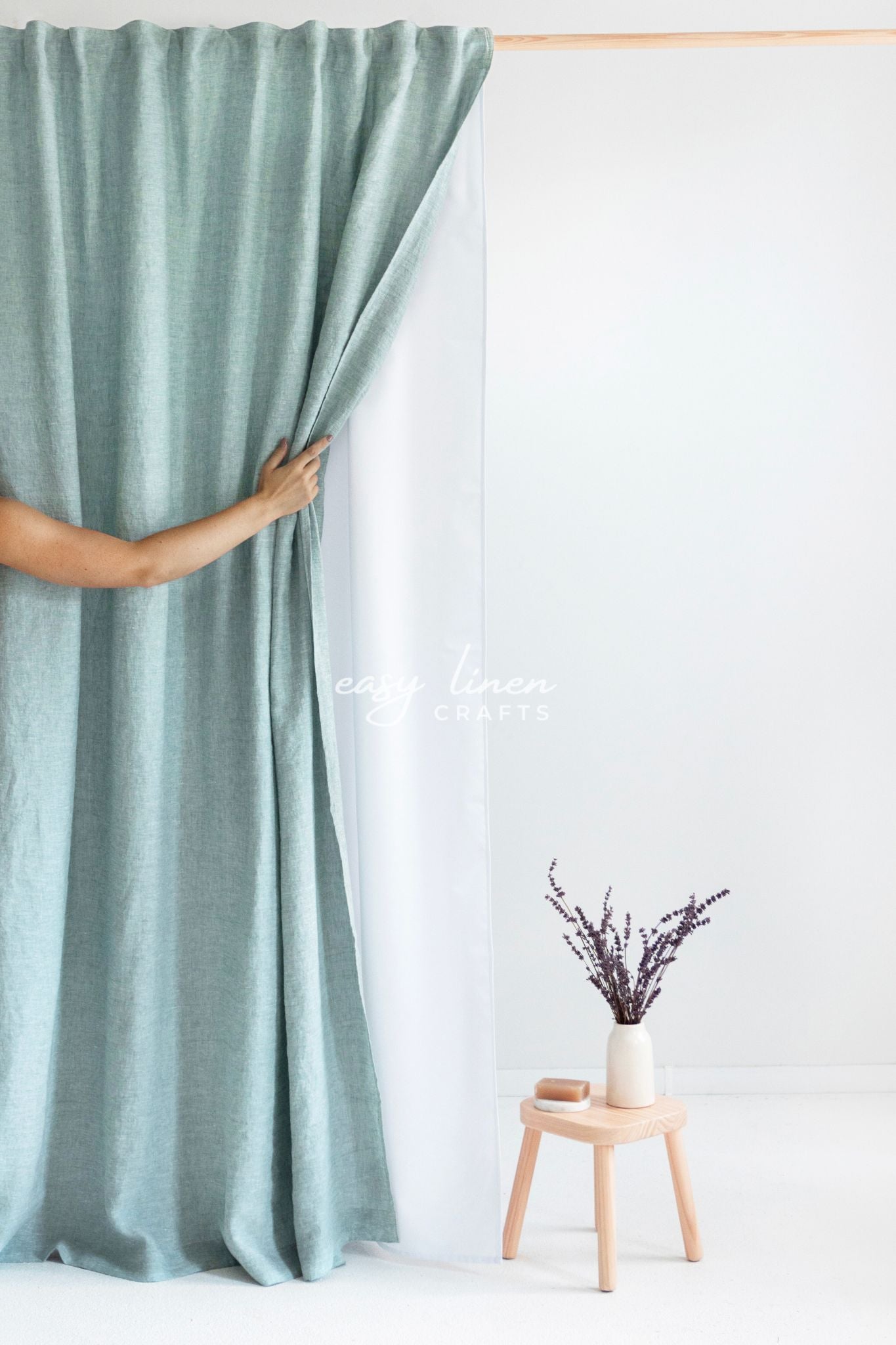 Person holding a green shower curtain with a white background and a small wooden stool with a vase.