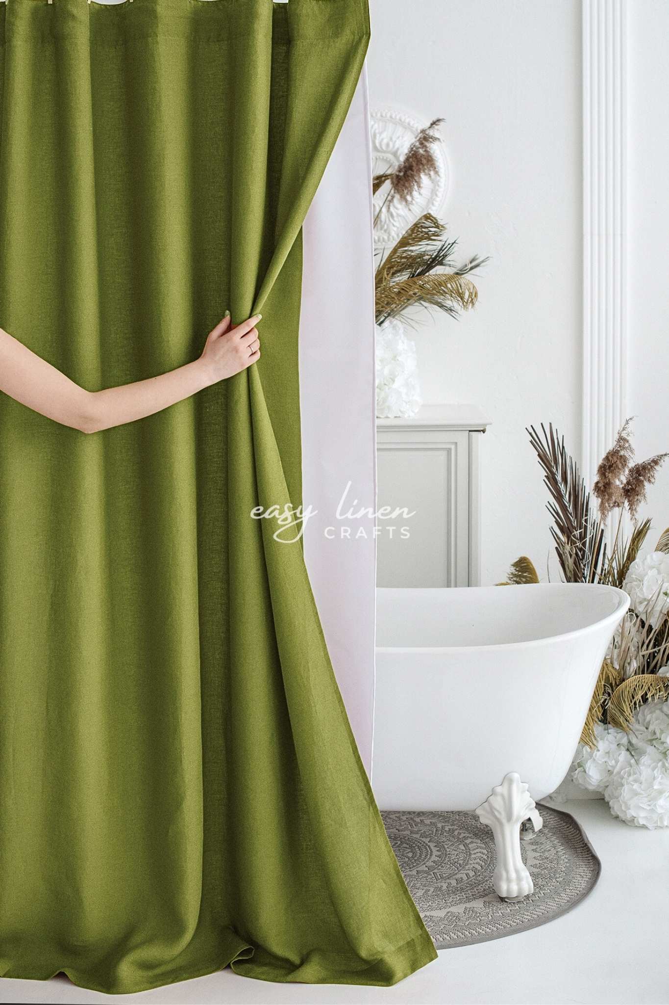 Green linen shower curtain being held open in a bathroom with a white bathtub and decorative elements.