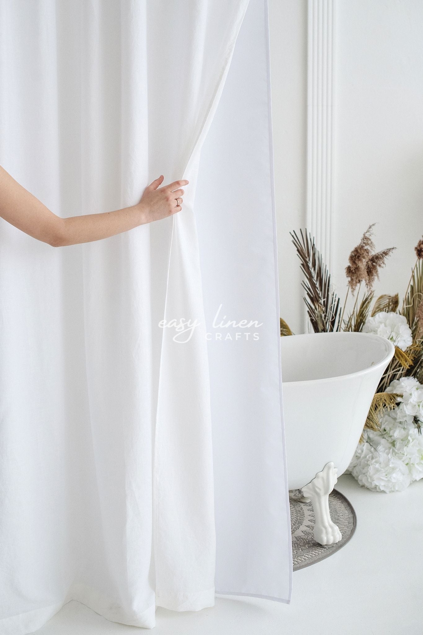 White shower curtain being pulled back to reveal a freestanding bathtub with decorative elements.
