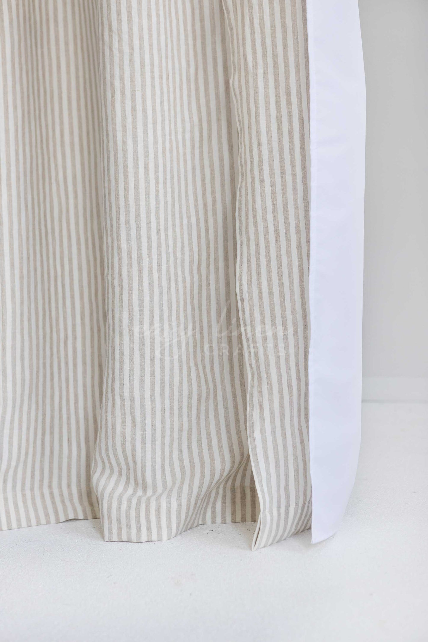 Close-up of a curtain panel with vertical beige and white stripes, showing the fabric texture and a white backing or inner panel.