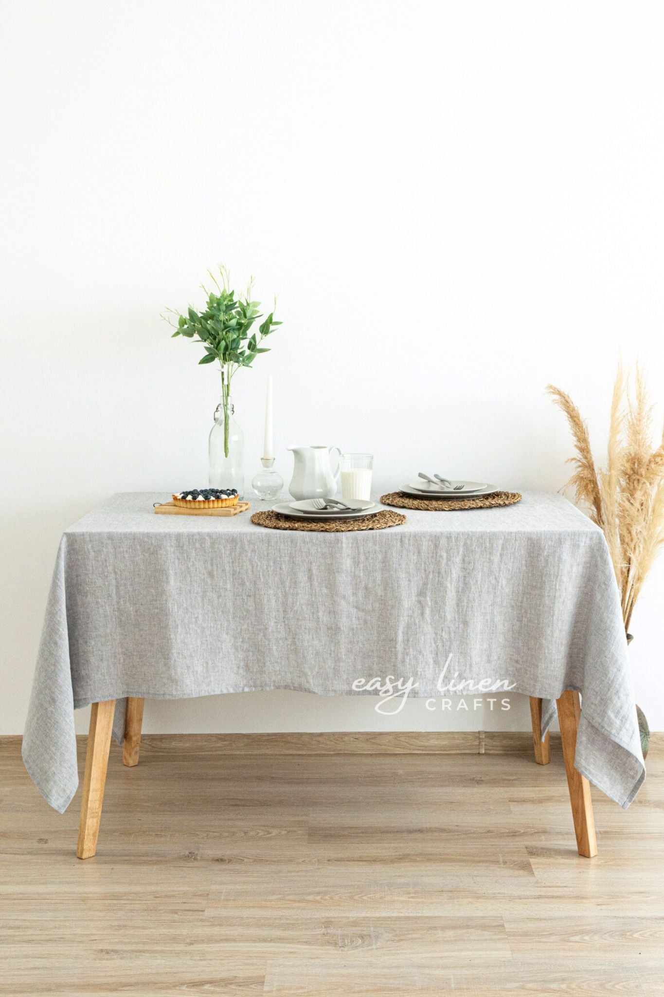 Table set with a gray tablecloth, plates, and a vase on a wooden floor.