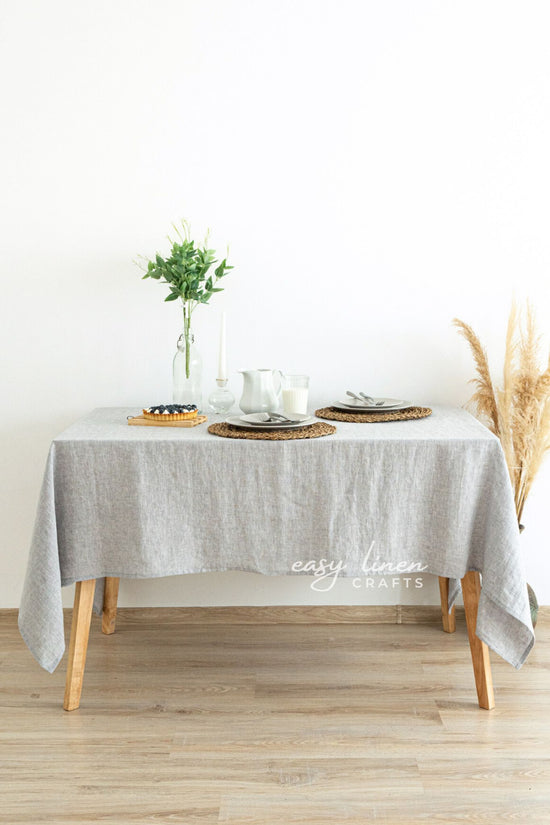 Table set with a gray tablecloth, plates, and a vase on a wooden floor.