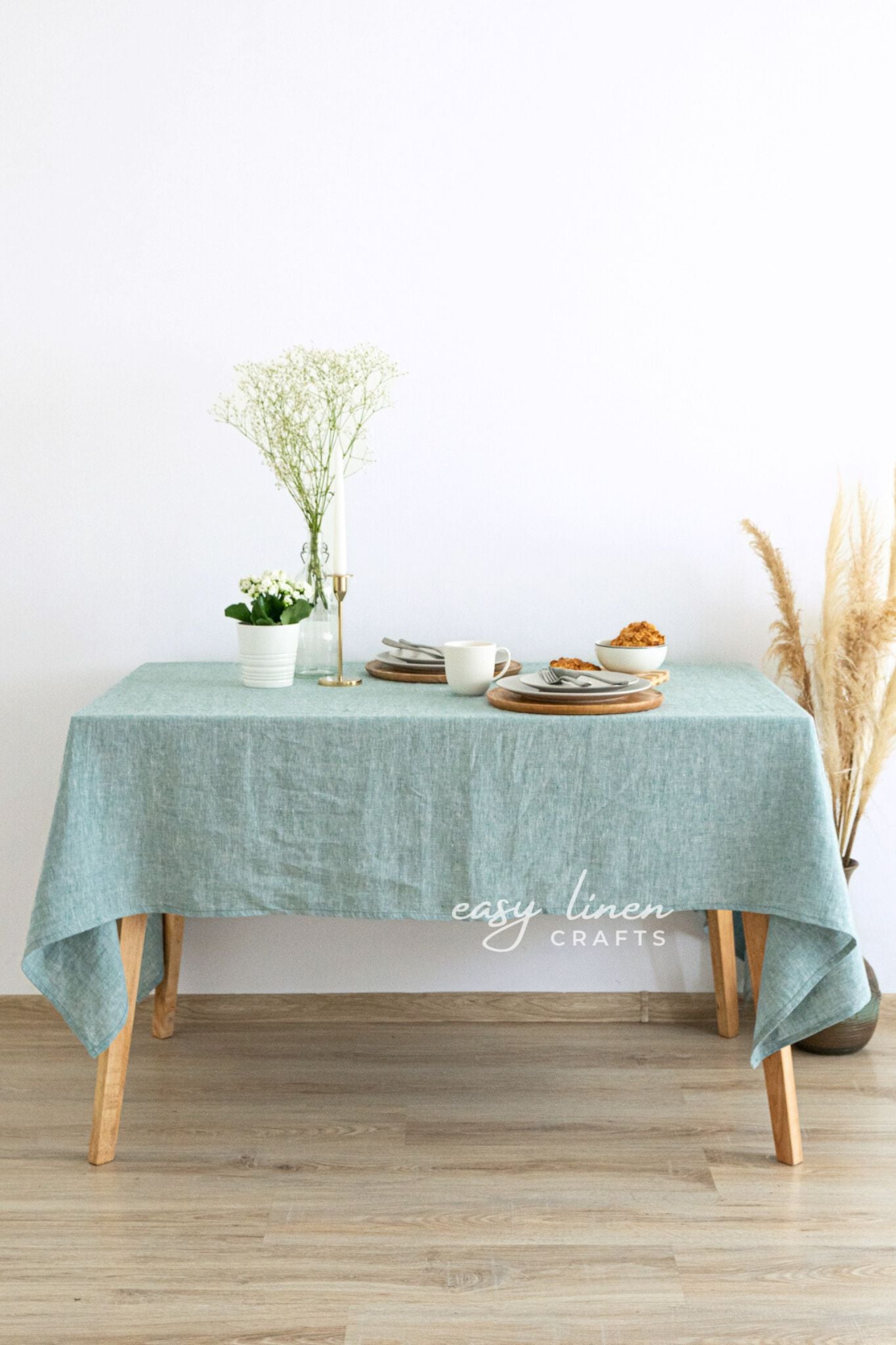 Table with a green tablecloth, plates, and a vase on a wooden floor.