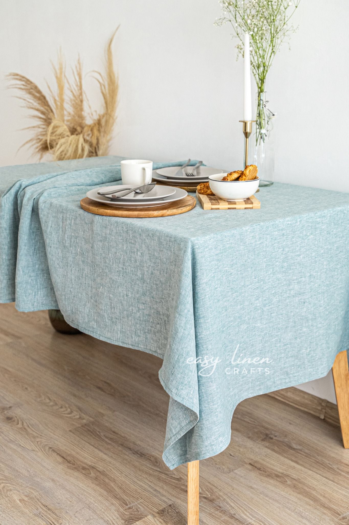Table setting with a light green tablecloth, plates, and cutlery on a wooden floor.