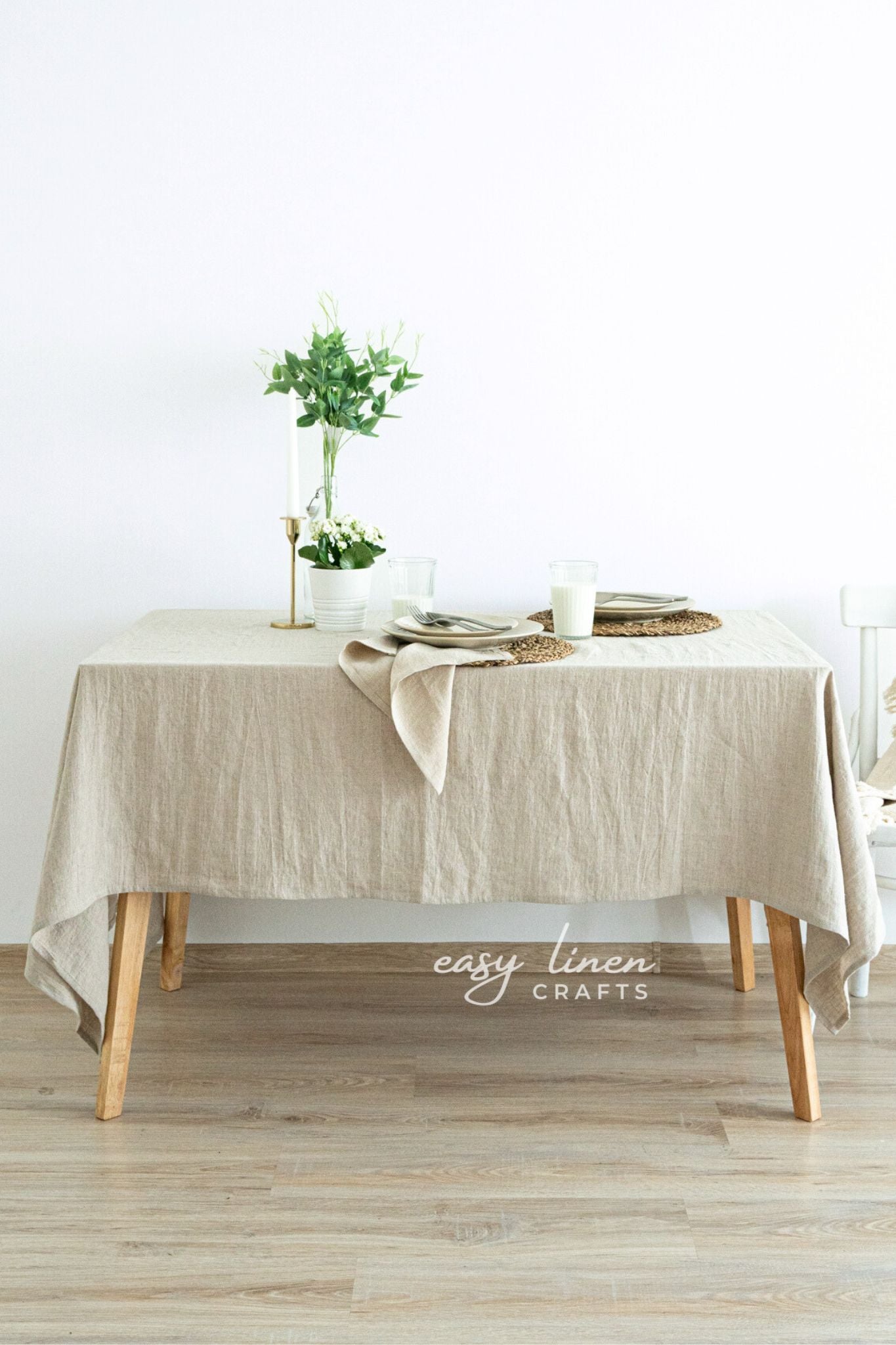 Beige linen tablecloth on a wooden table with minimal decor against a white wall.