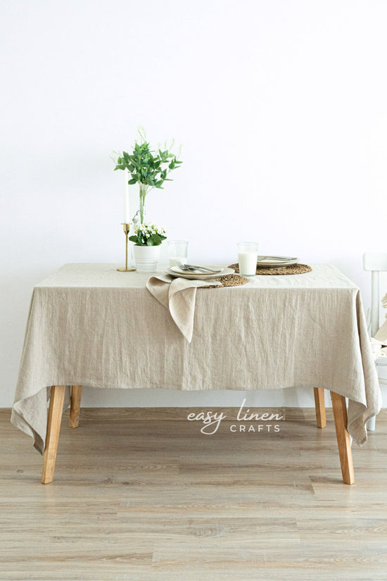Beige linen tablecloth on a wooden table with minimal decor against a white wall.