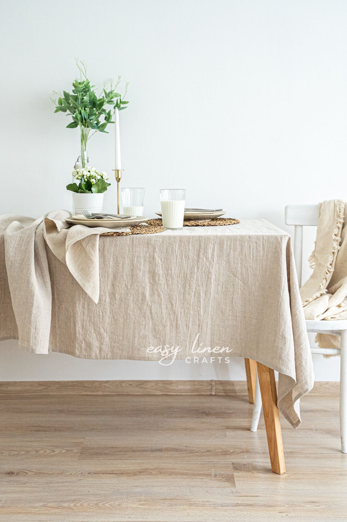 Beige linen tablecloth on a wooden table with a minimalistic setting.