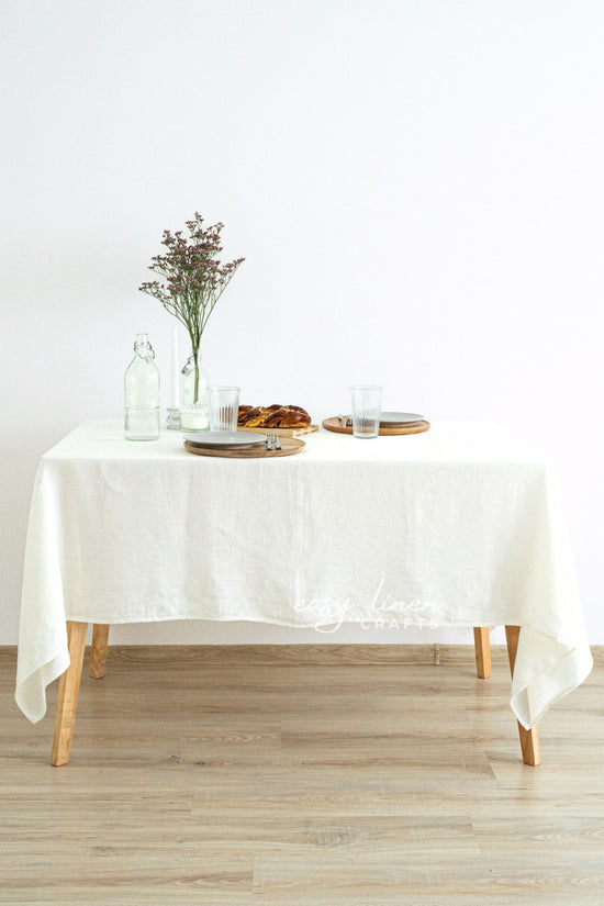 Dining table with a off white tablecloth, plates, and a vase on a wooden floor.