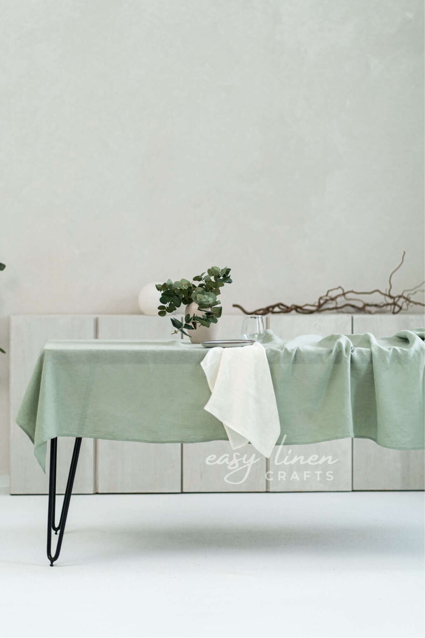 Mint green linen tablecloth on a table with a white wall background, featuring 'easy linen crafts' branding.