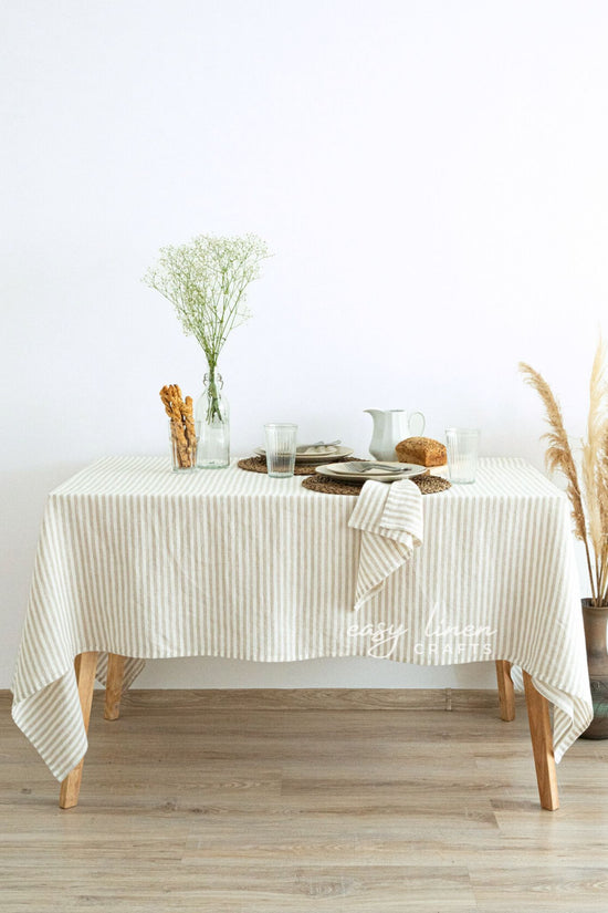 Table with a striped linen tablecloth, decorative items, and a vase on a light wooden floor.