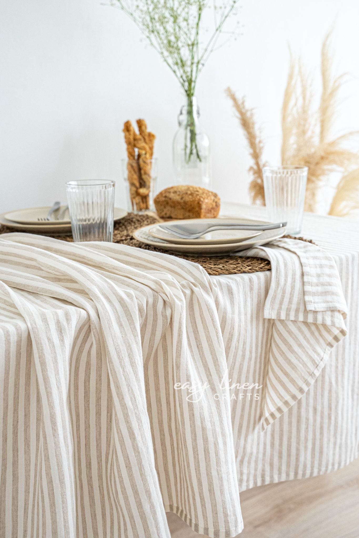Dining table set with striped linen tablecloth, plates, glasses, and bread.