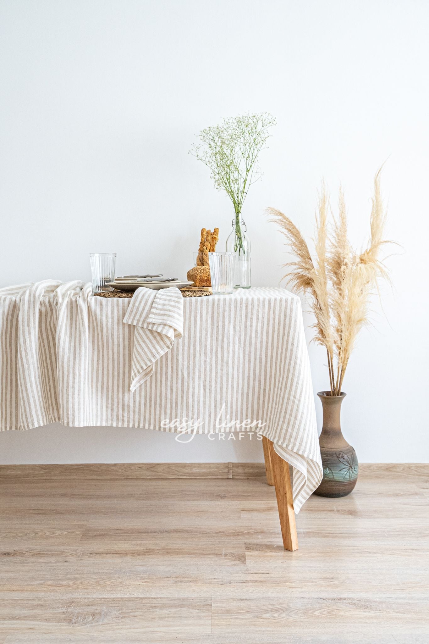 Dining table with a striped linen tablecloth, vase with flowers, and decorative items against a white wall.