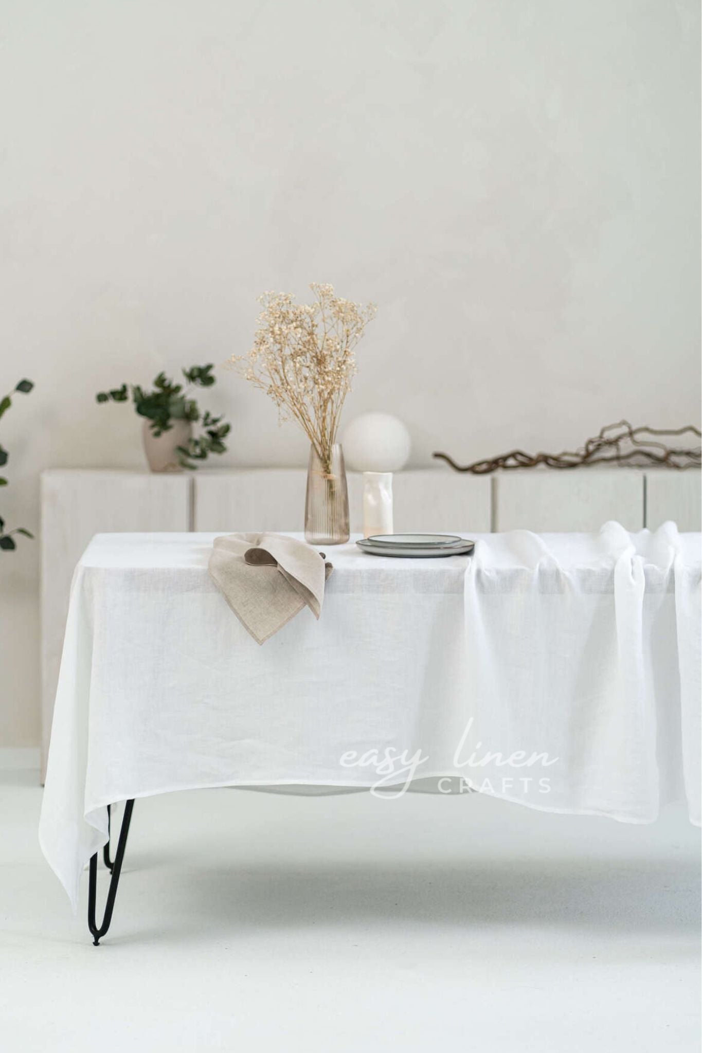 White tablecloth on a table with minimal decor against a white wall.