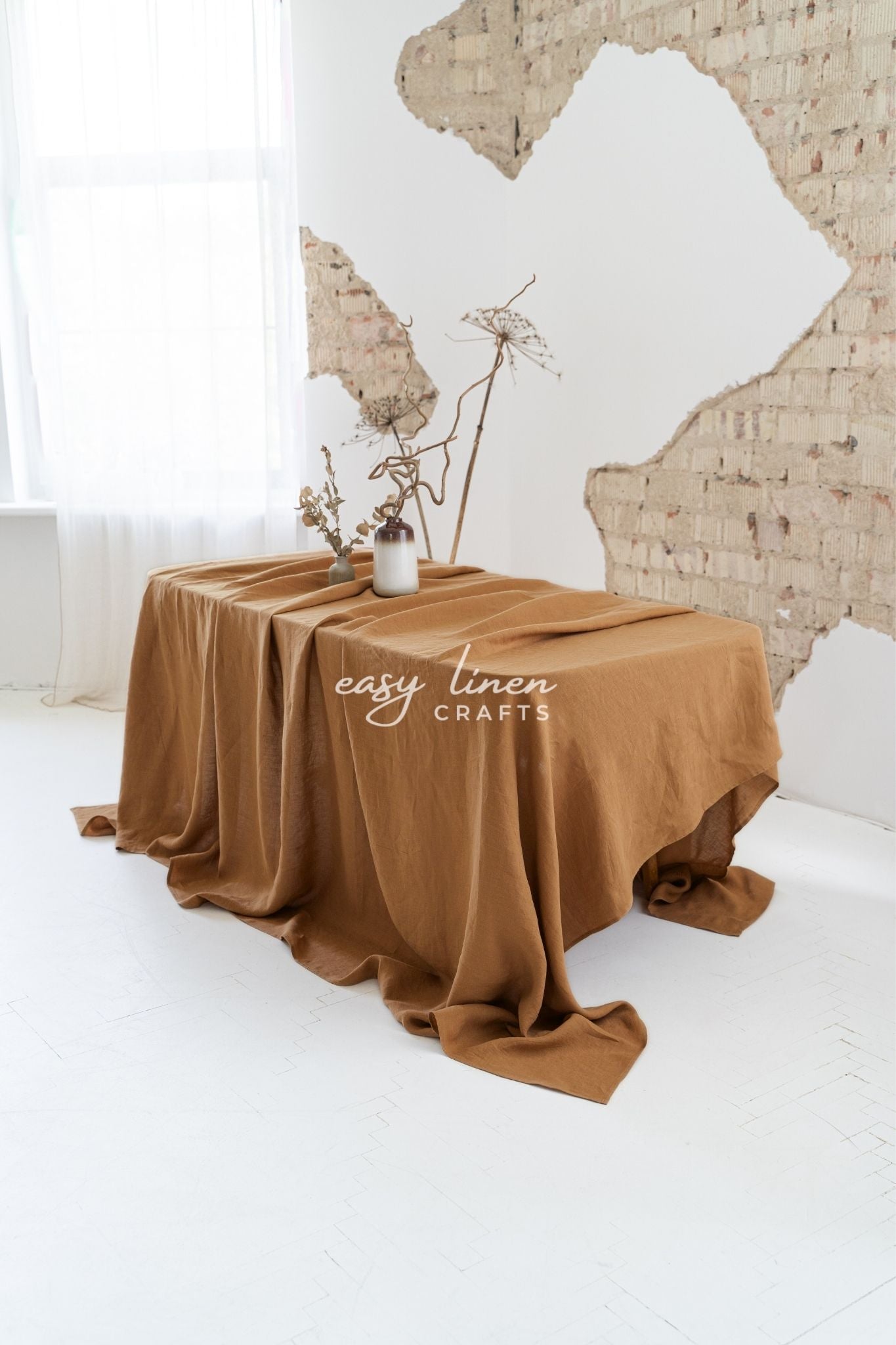 Brown linen draped over a table with a white curtain and brick wall in the background, featuring 'easy linen crafts' branding.