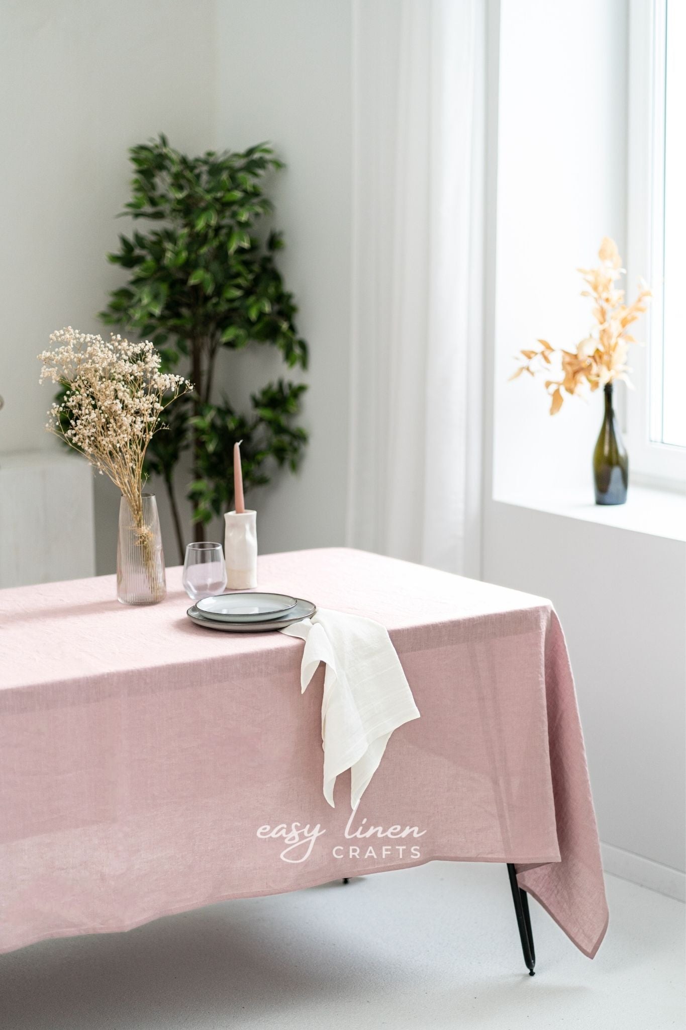Pink linen tablecloth on a table with decorative items in a bright room.