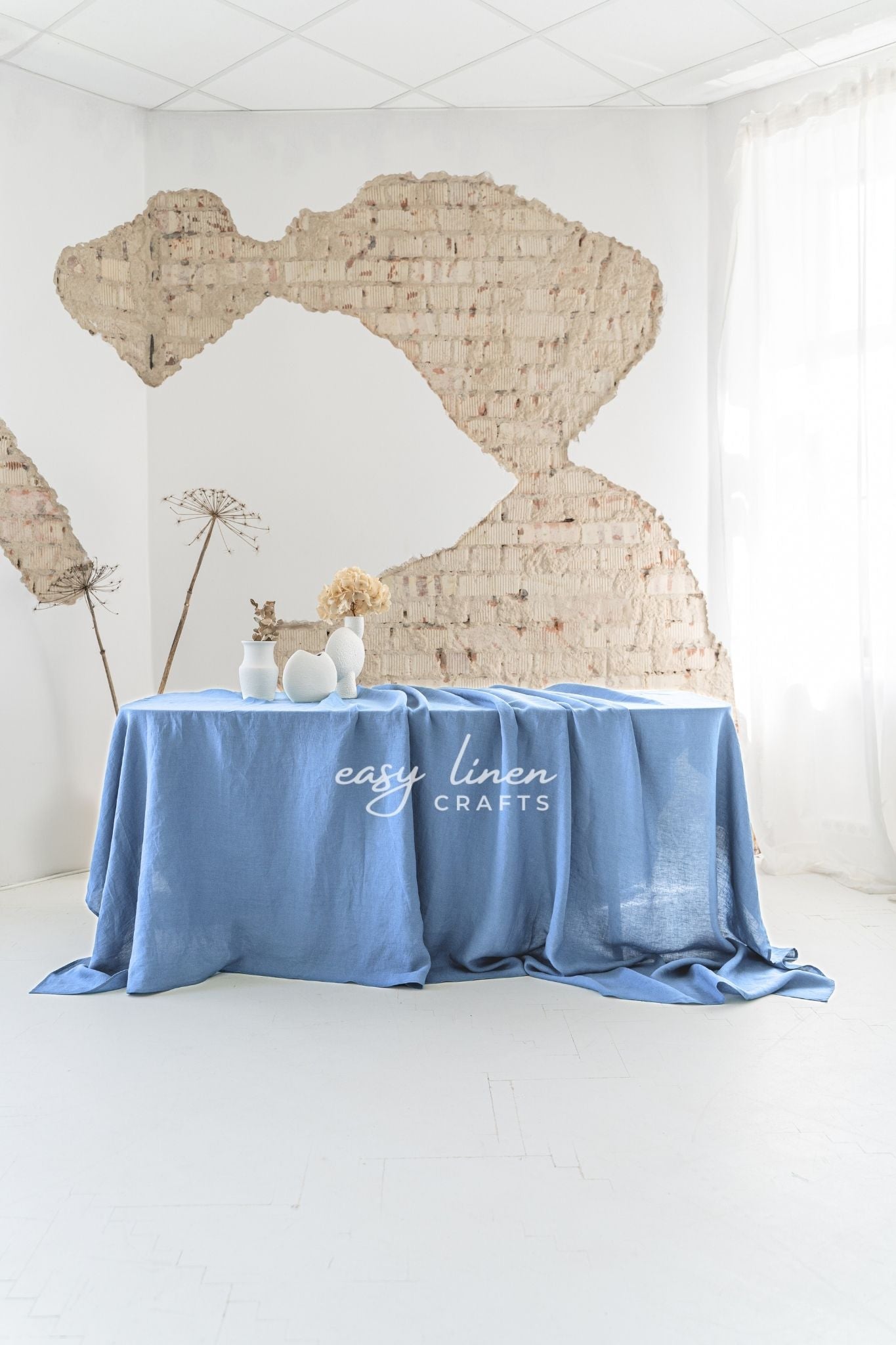 Blue linen tablecloth on a table with decorative items against a textured wall, featuring 'easy linen crafts' branding.
