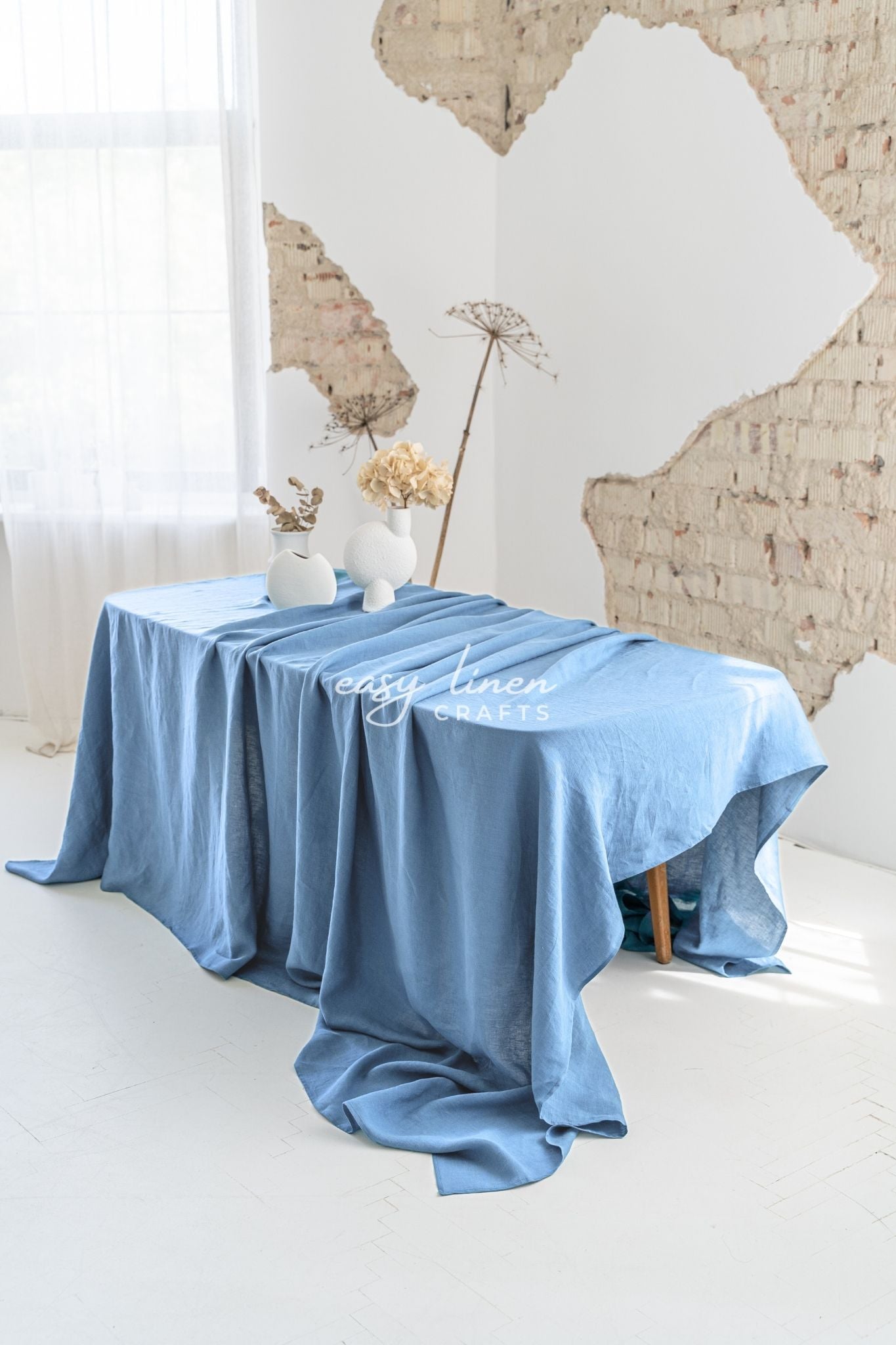Blue linen tablecloth on a table with decorative items against a brick wall.