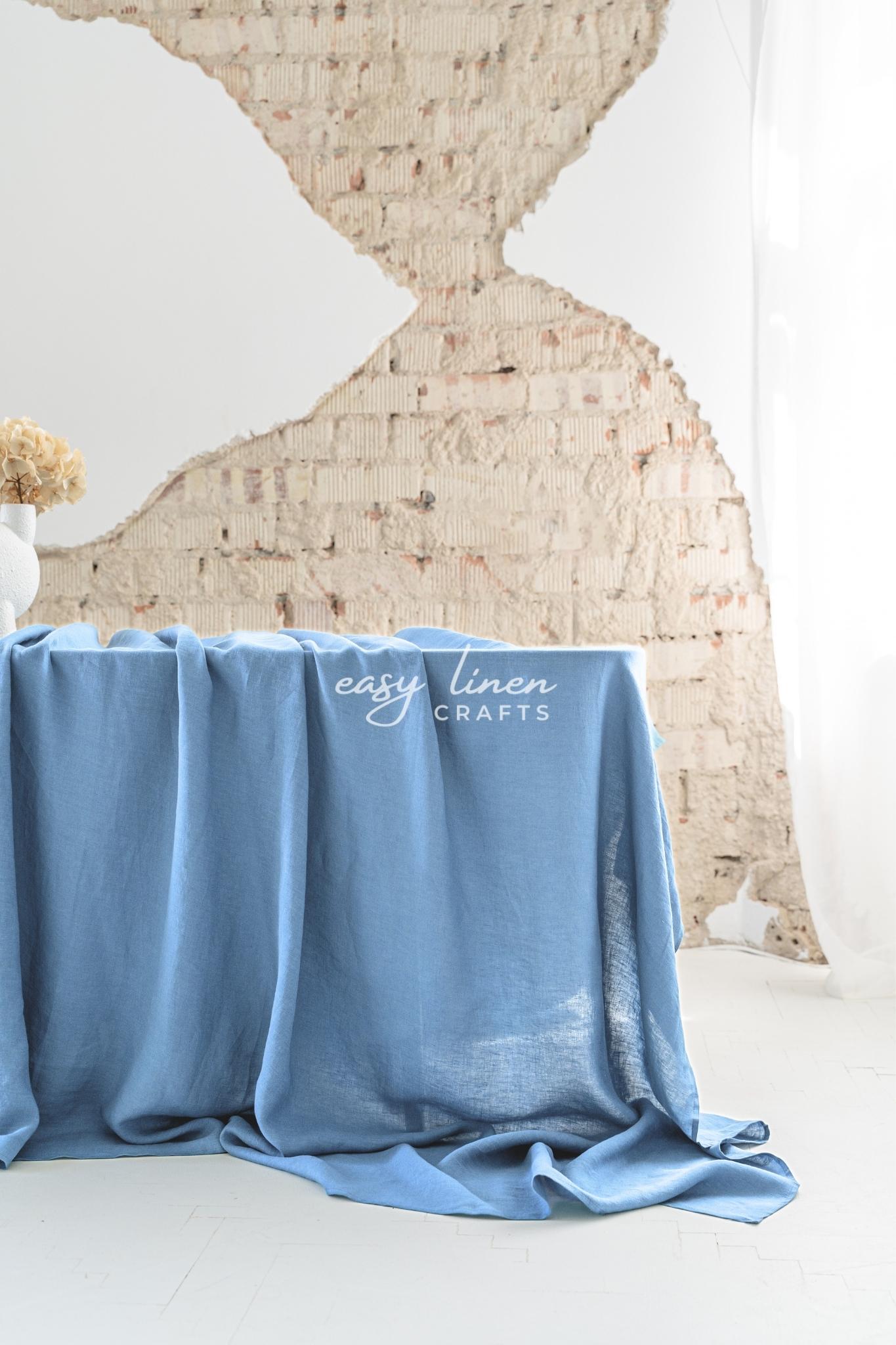 Blue tablecloth draped over a table with 'easy linen crafts' branding against a textured wall.