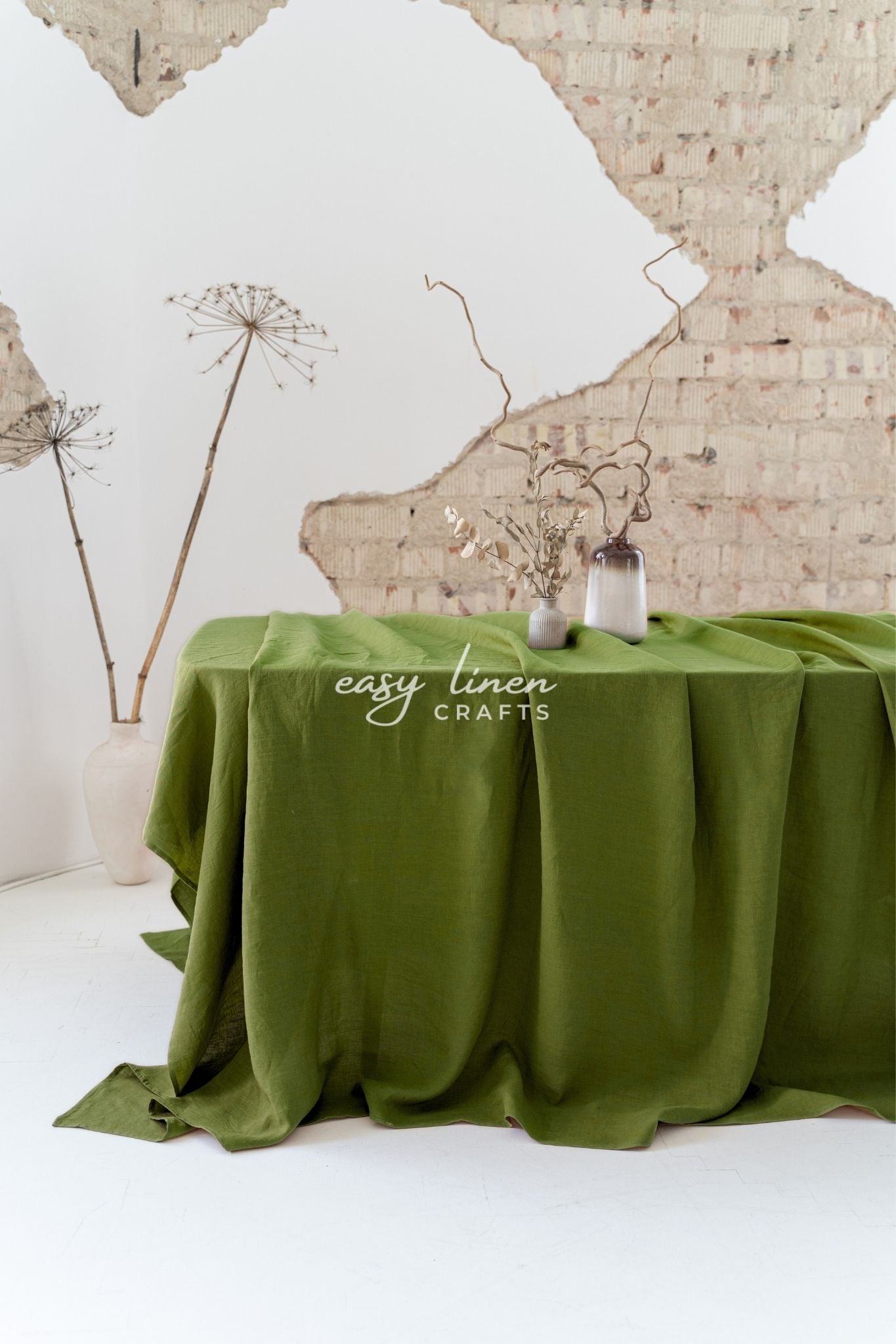 Green linen tablecloth on a table with decorative elements against a textured wall.