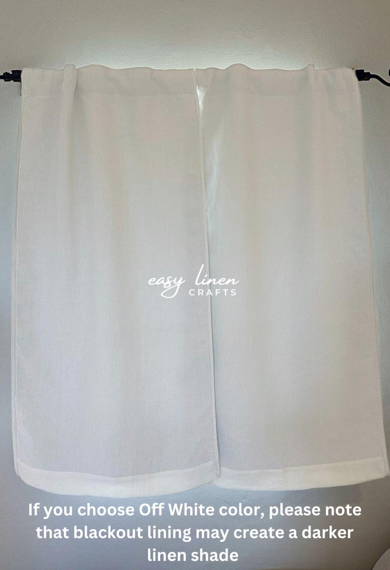 A pair of off-white curtain panels hanging from a black rod against a light wall, with a watermark reading 'easy linen CRAFTS' and a note at the bottom explaining that the off-white color may appear darker due to blackout lining.
