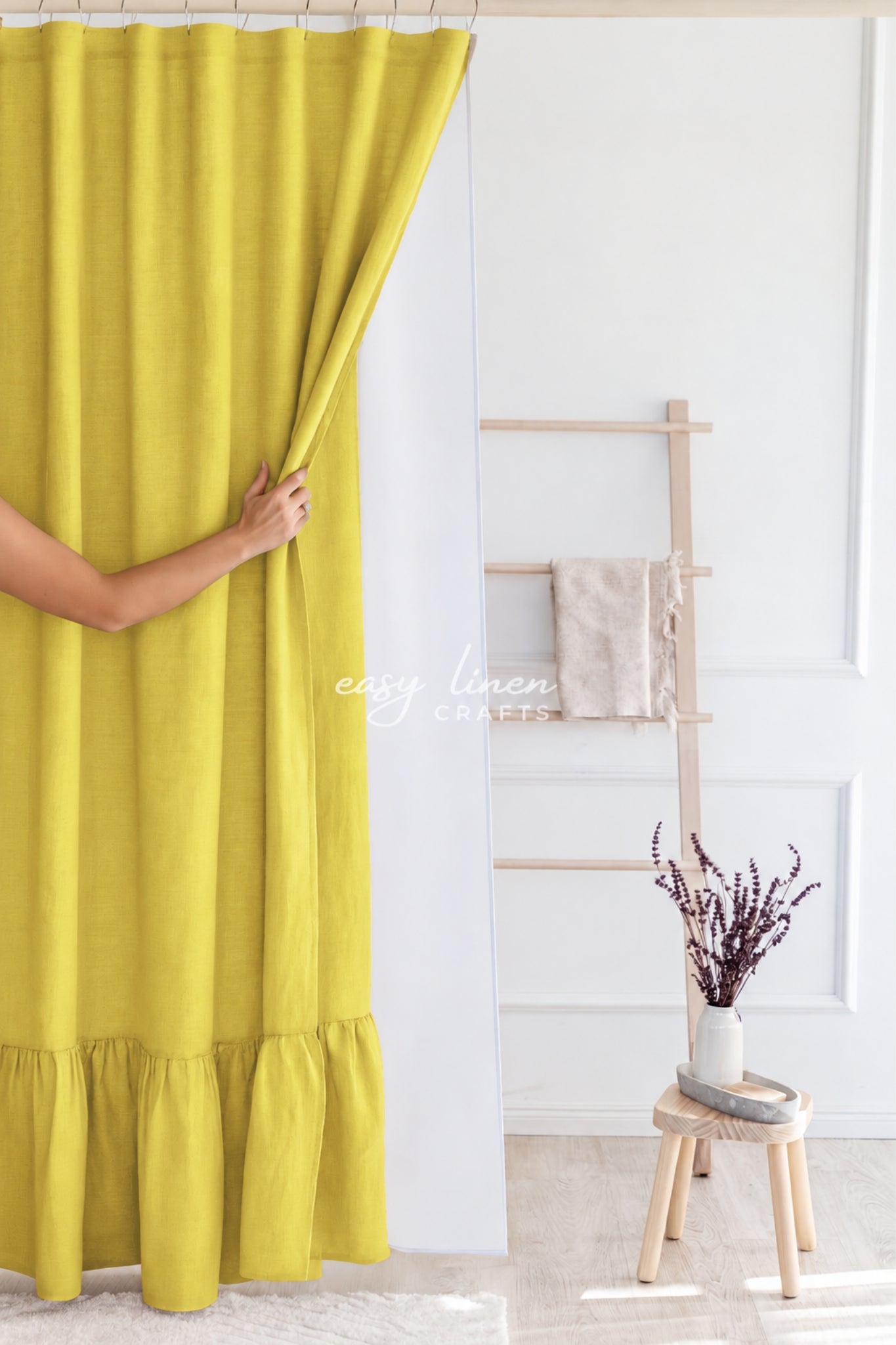 A person's arm and hand are shown pulling a bright yellow curtain to the side in a bright, modern room. The curtain has a ruffled hem and is held by a rod.
