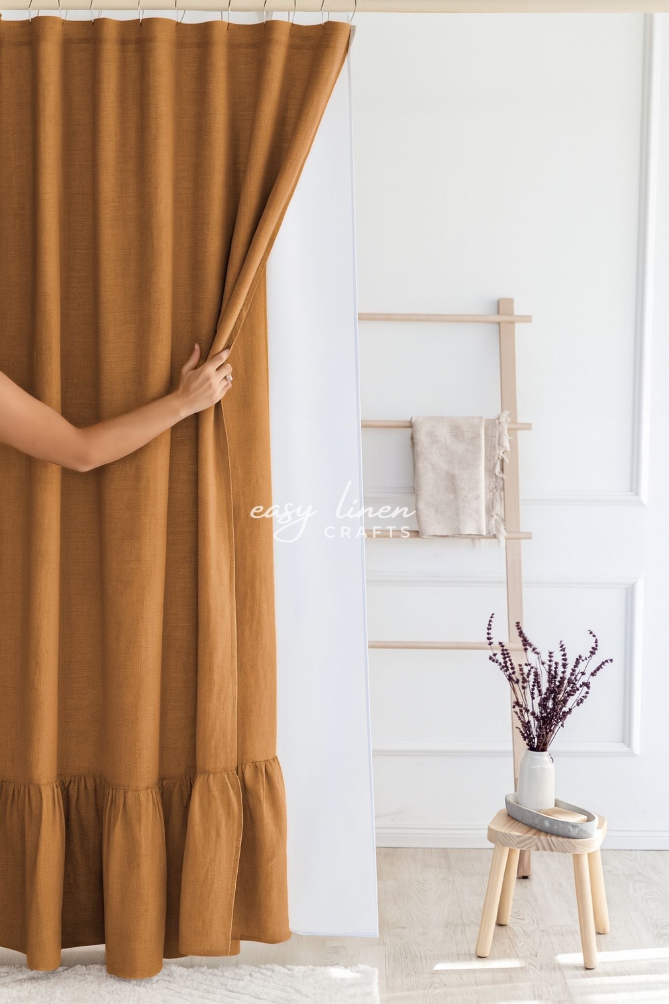 Person opening a mustard yellow shower curtain in a room with a wooden stool and plant.
