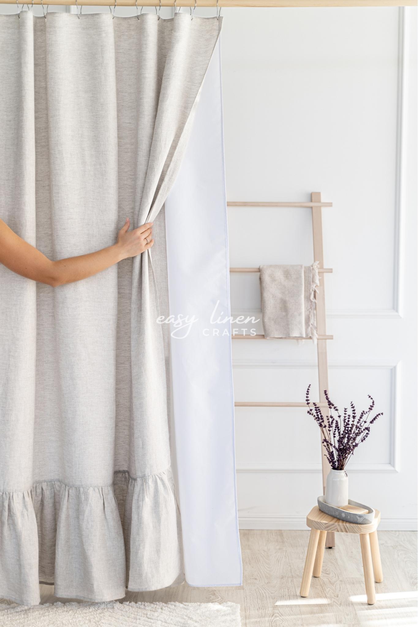 Person holding a natural light linen shower curtain in a room with a wooden stool and decorative items