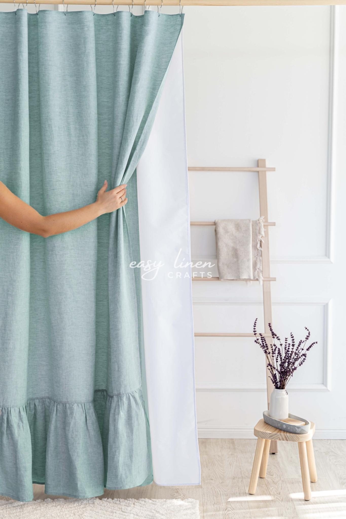 Person holding a melange green shower curtain in a room with a wooden stool and decorative items.