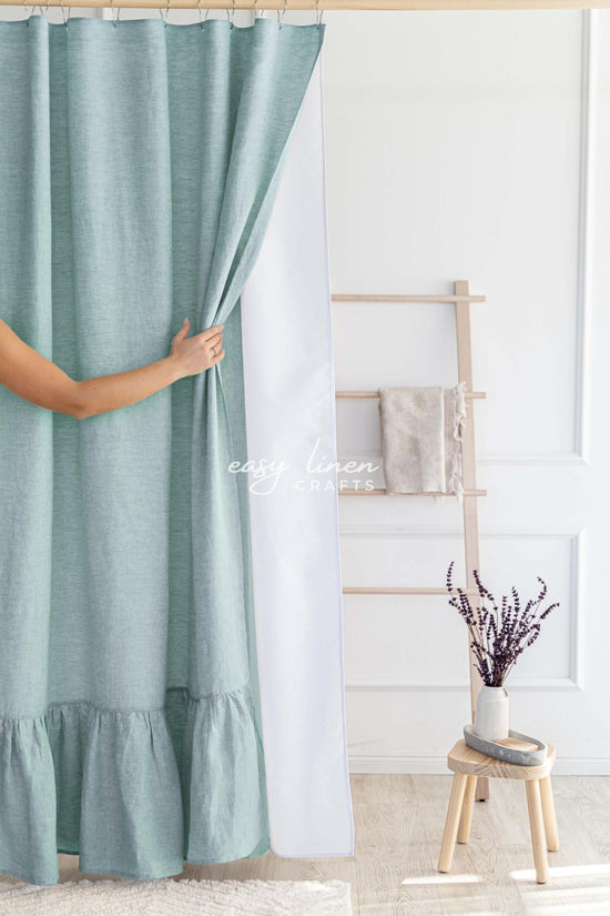 Person holding a melange green shower curtain in a room with a wooden stool and decorative items.