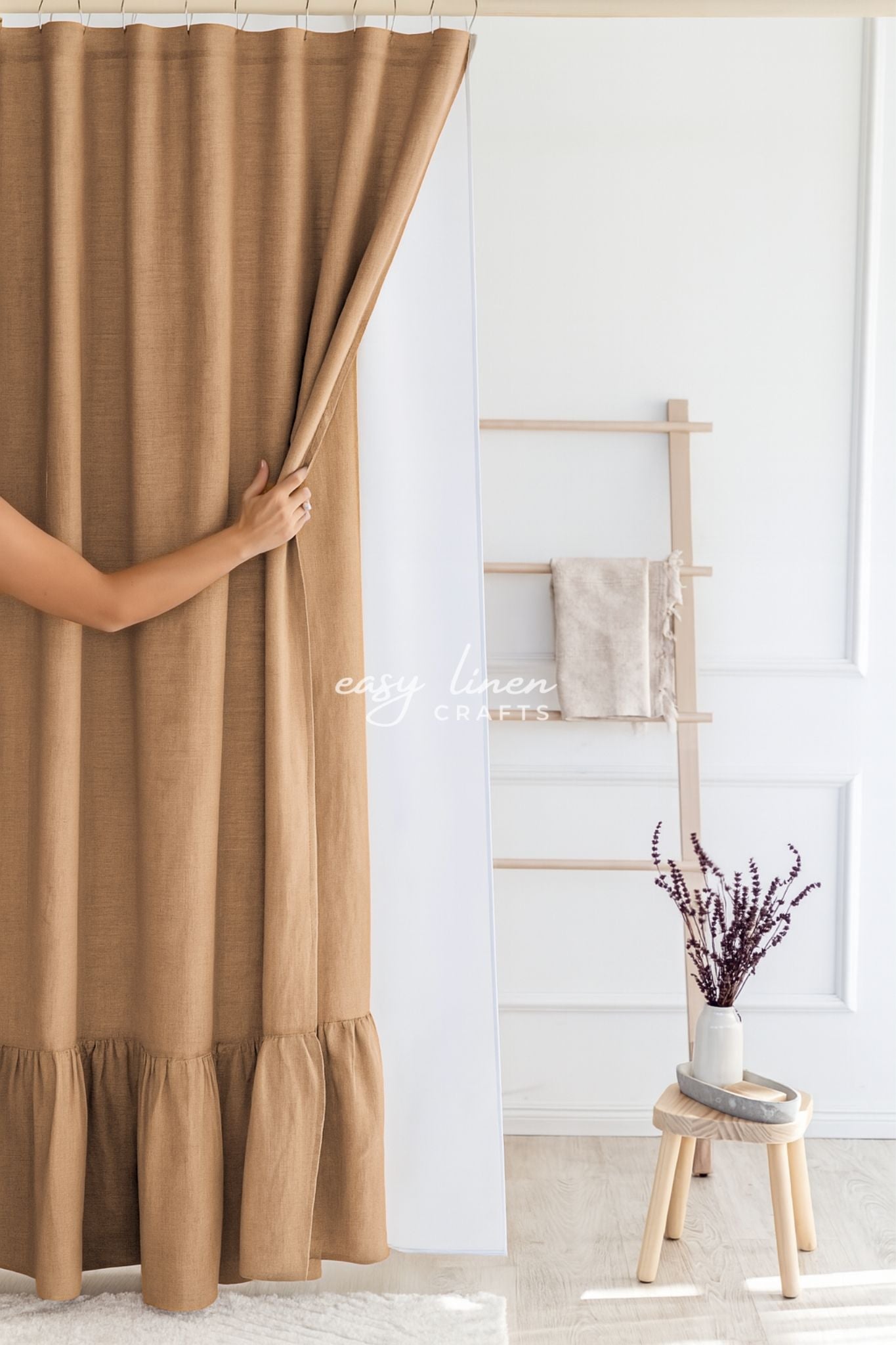 Brown shower curtain being pulled open in a room with a wooden stool and plant.