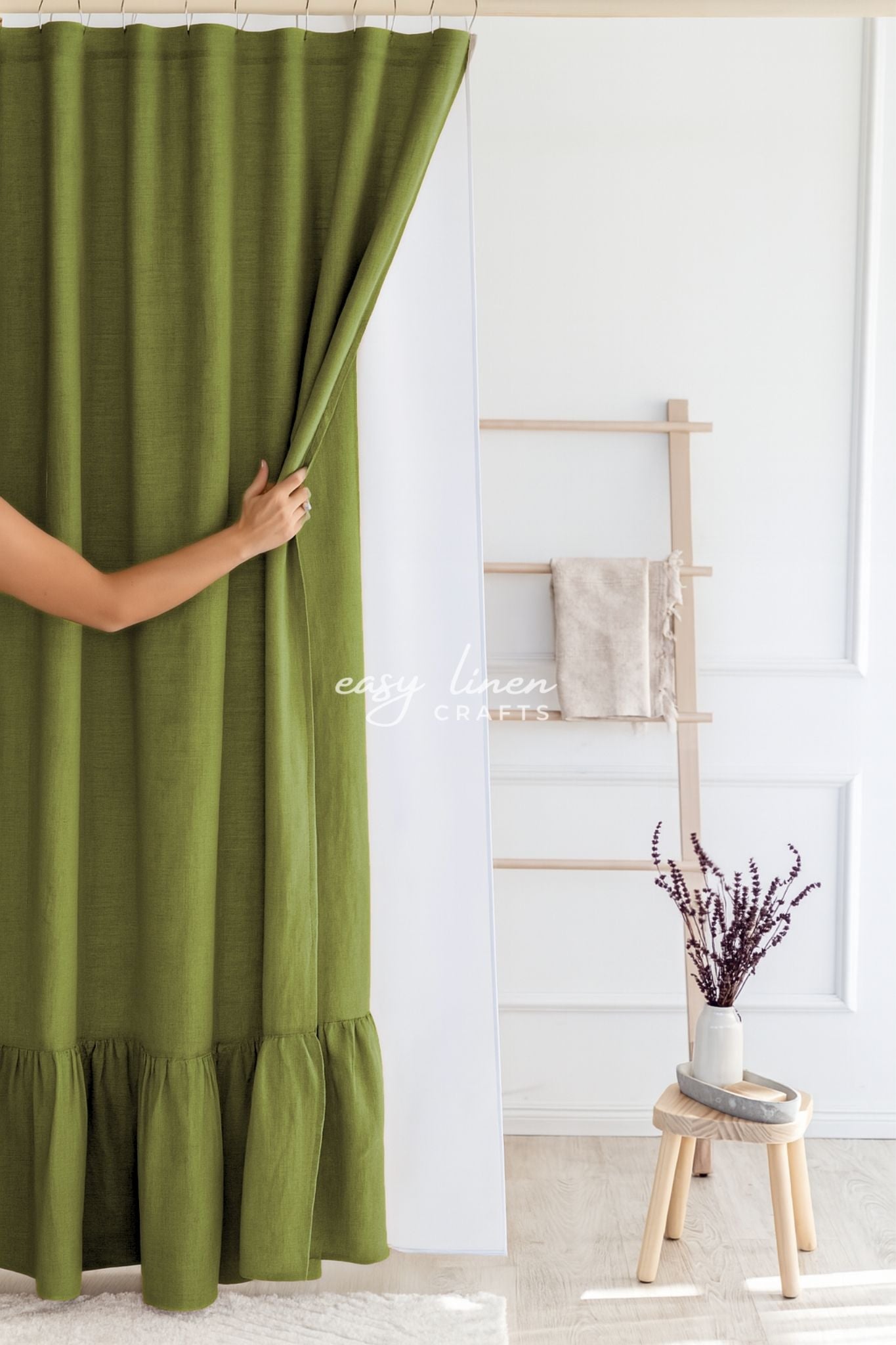 Moss green linen shower curtain in a room with a wooden stool and a plant.
