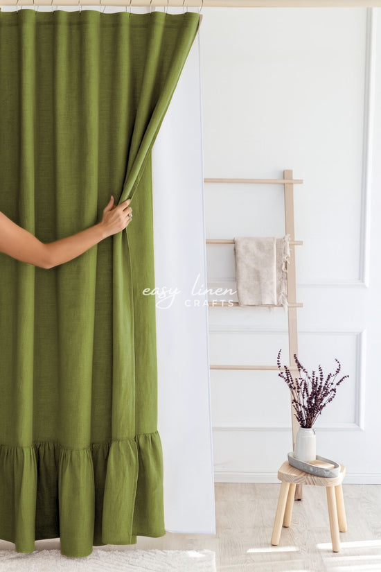 Moss green linen shower curtain in a room with a wooden stool and a plant.