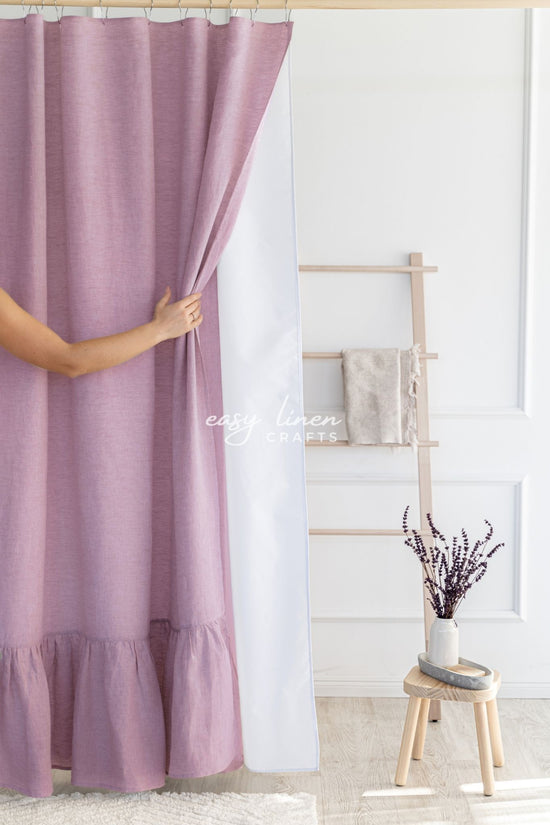 Person holding a dusty rose shower curtain in a room with a wooden stool and decorative items.