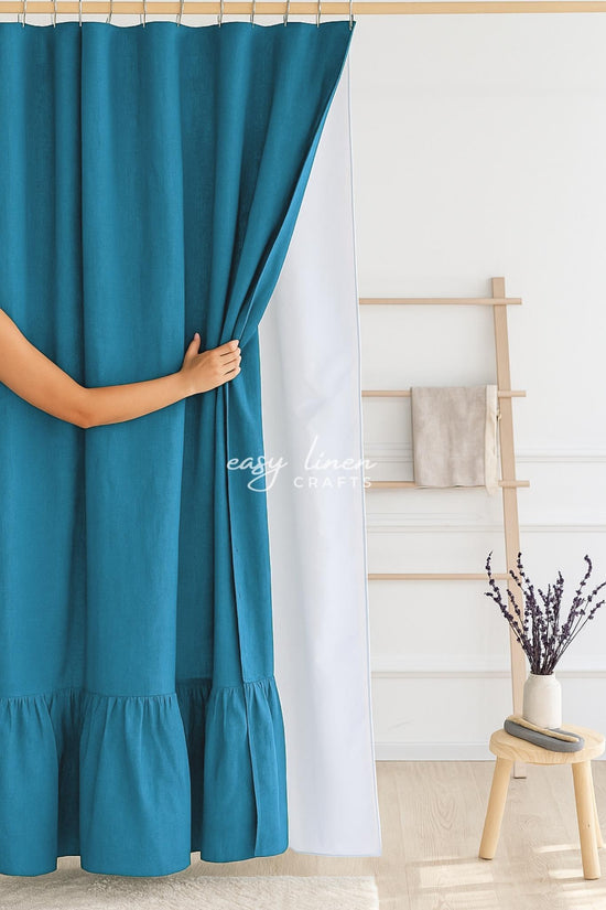Teal blue shower curtain being held open with a minimal background
